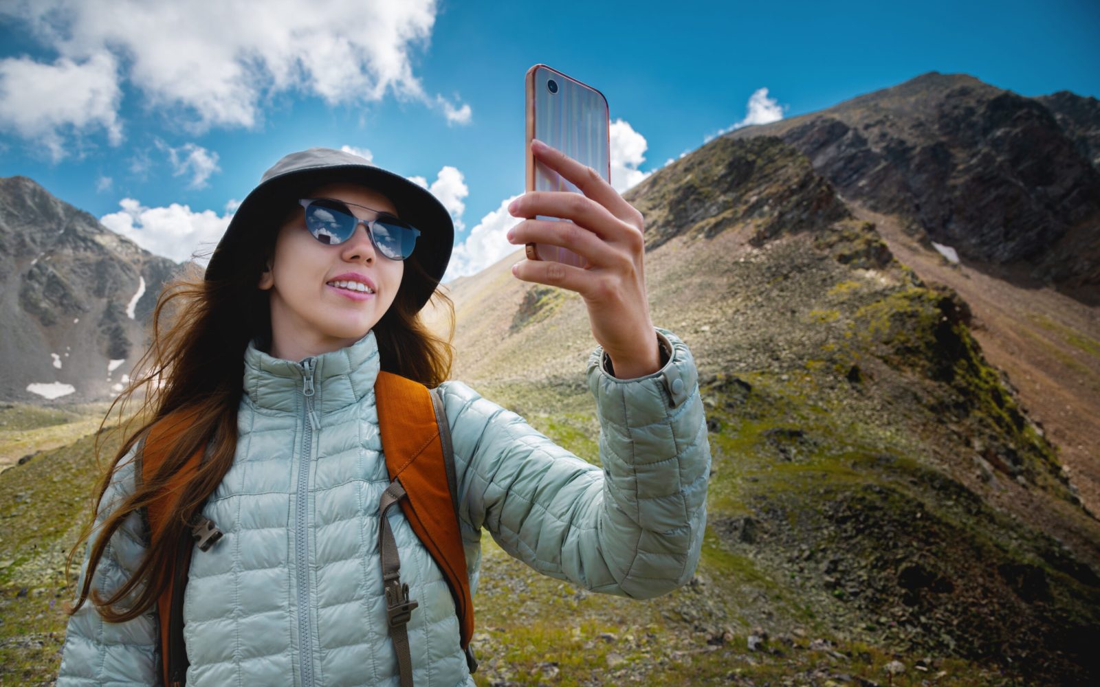 a happy girl takes a selfie against the backdrop of green and snow-capped mountains. hiking, backpacking, tourism.